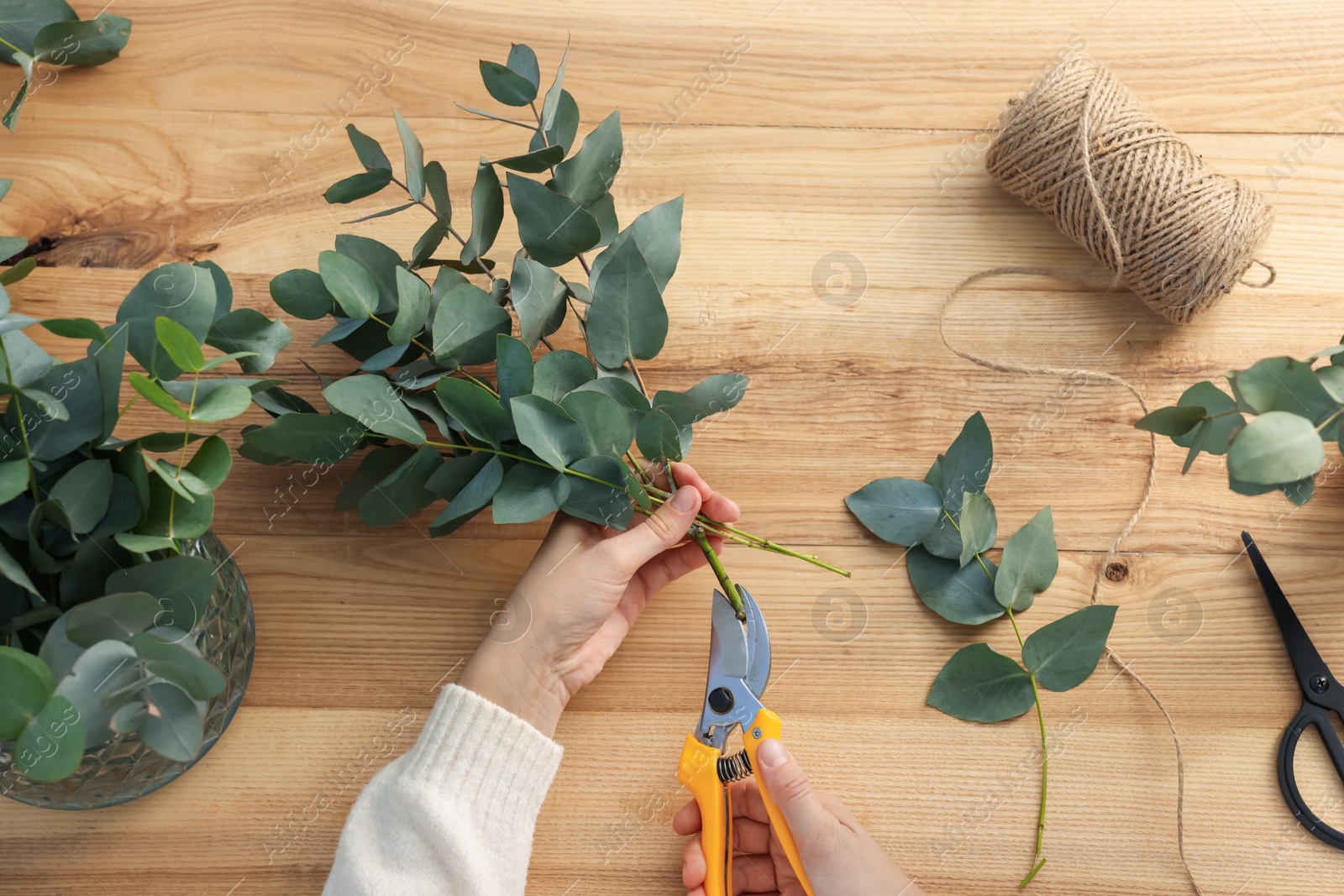 Florist making beautiful bouquet of eucalyptus branches at wooden table, top view Photo of Florist making beautiful bouquet of eucalyptus branches at wooden table, top view