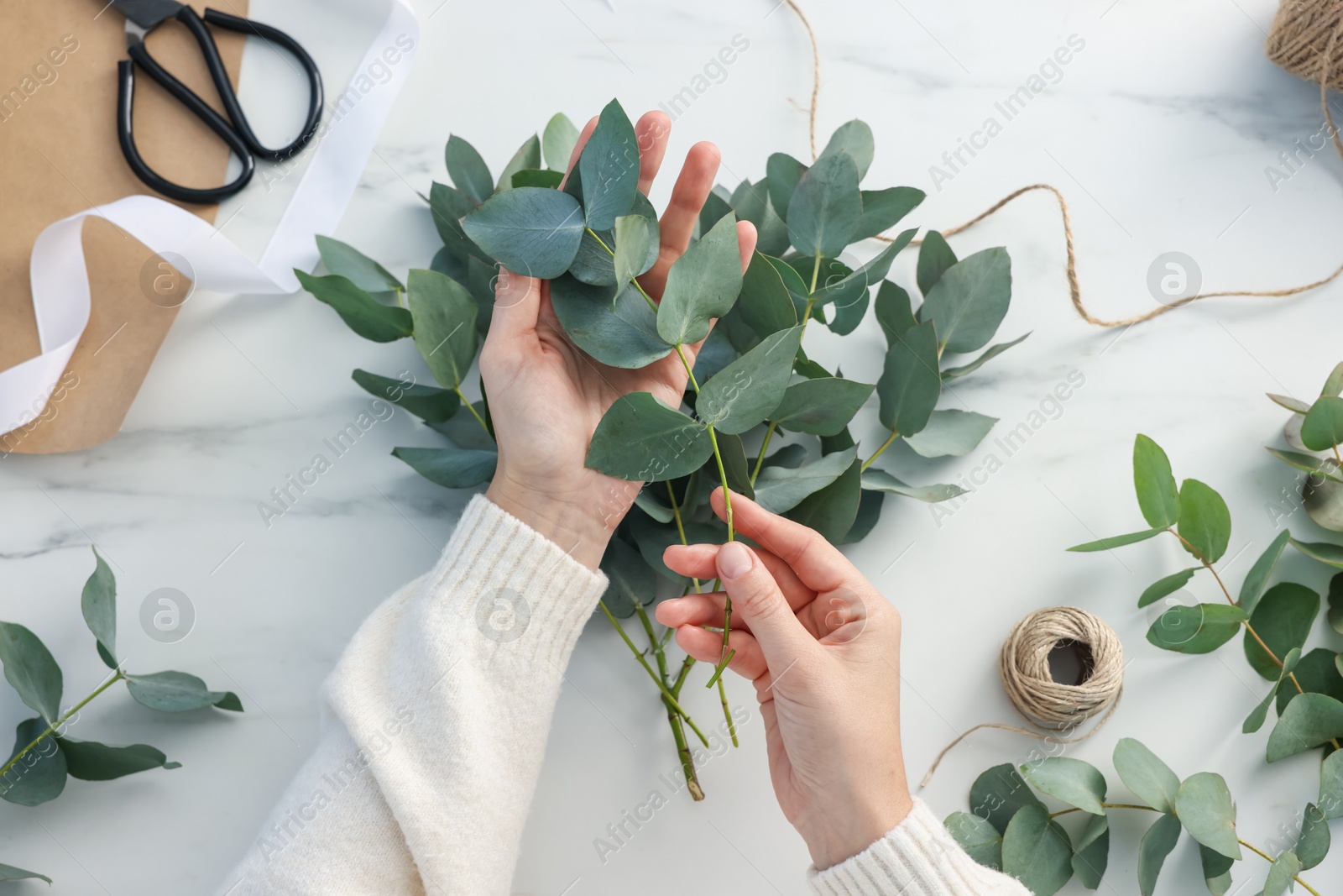 Florist making beautiful bouquet of eucalyptus branches at white marble table, top view Photo of Florist making beautiful bouquet of eucalyptus branches at white marble table, top view