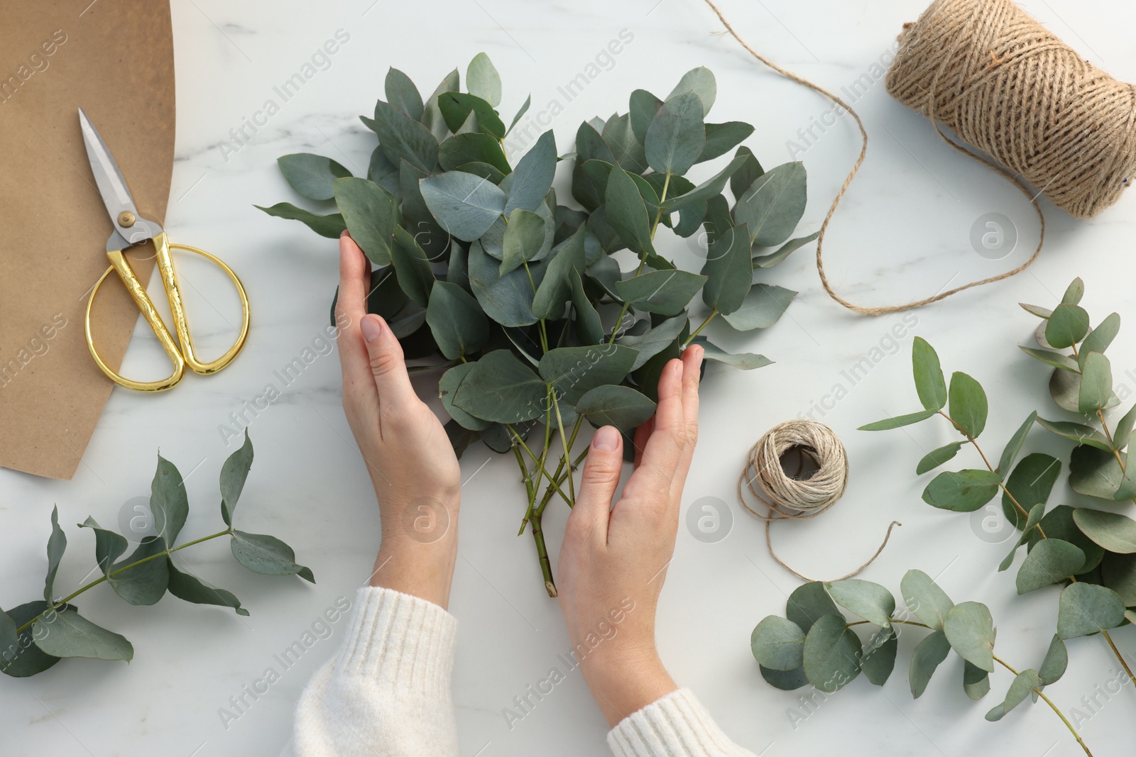 Florist making beautiful bouquet of eucalyptus branches at white marble table, top view Photo of Florist making beautiful bouquet of eucalyptus branches at white marble table, top view