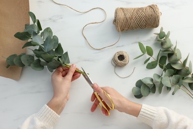 Photo of Florist making beautiful bouquet of eucalyptus branches at white marble table, top view