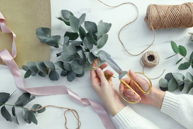 Photo of Florist making beautiful bouquet of eucalyptus branches at white marble table, top view