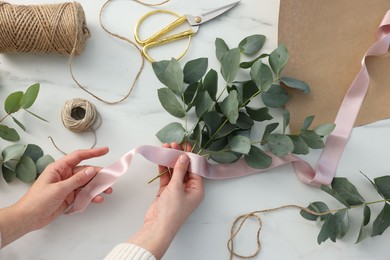 Photo of Florist making beautiful bouquet of eucalyptus branches at white marble table, top view