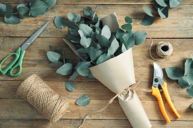 Photo of Florist. Eucalyptus branches, threads, pruner, wrapping paper and scissors on wooden table, flat lay