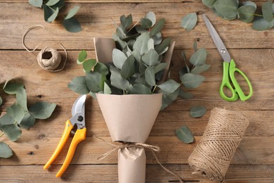 Photo of Florist. Eucalyptus branches, threads, pruner, wrapping paper and scissors on wooden table, flat lay