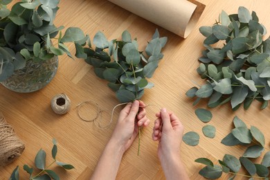 Photo of Florist making beautiful bouquet of eucalyptus branches at wooden table, top view
