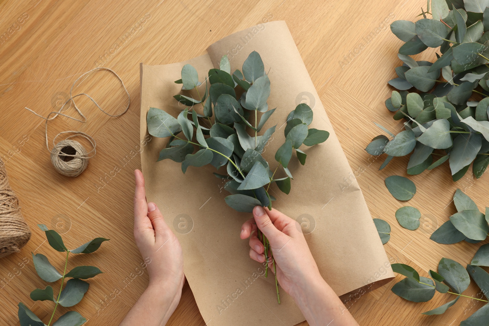Florist making beautiful bouquet of eucalyptus branches at wooden table, top view Photo of Florist making beautiful bouquet of eucalyptus branches at wooden table, top view