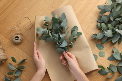 Photo of Florist making beautiful bouquet of eucalyptus branches at wooden table, top view