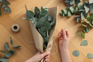 Photo of Florist making beautiful bouquet of eucalyptus branches at wooden table, top view