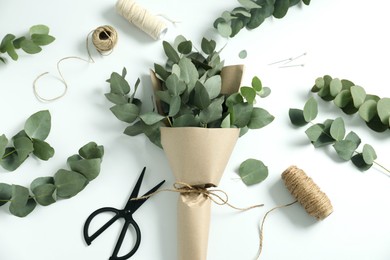 Photo of Florist. Eucalyptus branches, threads and scissors on white table, flat lay