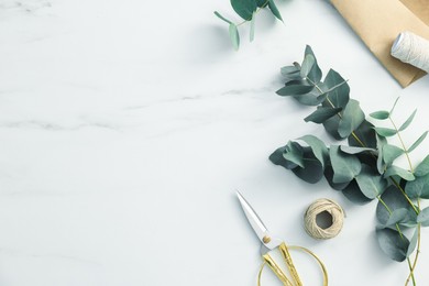 Photo of Florist. Eucalyptus branches, threads and scissors on white marble table, flat lay. Space for text