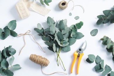 Photo of Florist. Eucalyptus branches, threads, pruner and ribbon on white table, flat lay