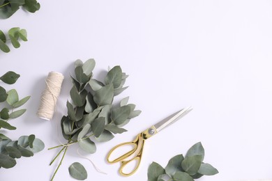 Photo of Florist. Eucalyptus branches, thread and scissors on white table, flat lay. Space for text