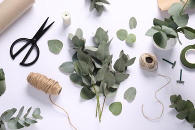 Photo of Florist. Eucalyptus branches, threads, scissors and wrapping paper on white table, flat lay