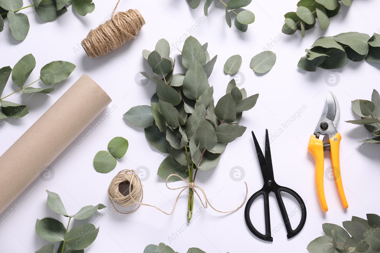Florist. Eucalyptus branches, threads, scissors, pruner and wrapping paper on white table, flat lay Photo of Florist. Eucalyptus branches, threads, scissors, pruner and wrapping paper on white table, flat lay