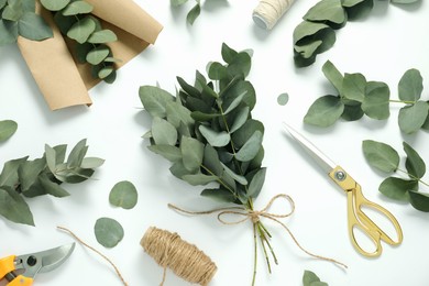 Photo of Florist. Eucalyptus branches, threads, scissors, pruner and wrapping paper on white table, flat lay