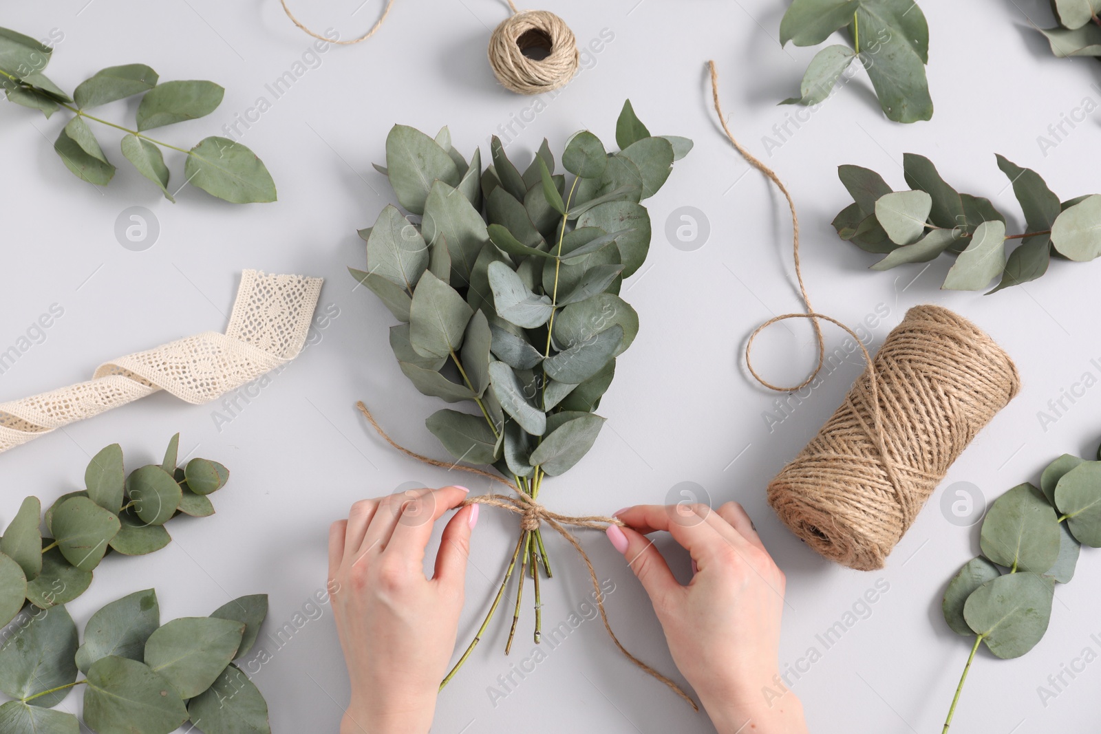 Florist making beautiful bouquet of eucalyptus branches at white table, top view Photo of Florist making beautiful bouquet of eucalyptus branches at white table, top view