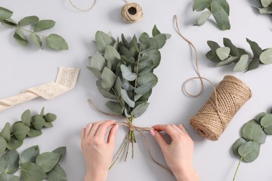 Photo of Florist making beautiful bouquet of eucalyptus branches at white table, top view