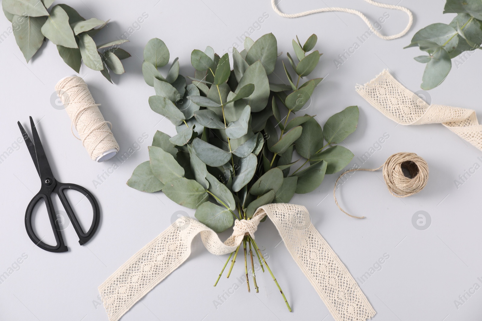 Florist. Eucalyptus branches, threads, scissors and ribbon on white table, flat lay Photo of Florist. Eucalyptus branches, threads, scissors and ribbon on white table, flat lay