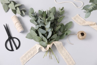 Photo of Florist. Eucalyptus branches, threads, scissors and ribbon on white table, flat lay