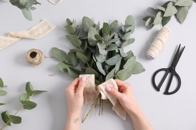 Photo of Florist making beautiful bouquet of eucalyptus branches at white table, top view