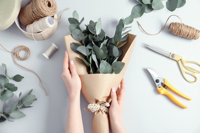 Photo of Florist making beautiful bouquet of eucalyptus branches at white table, top view