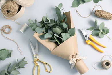 Photo of Florist. Eucalyptus branches, threads, scissors, pruner and wrapping paper on white table, flat lay