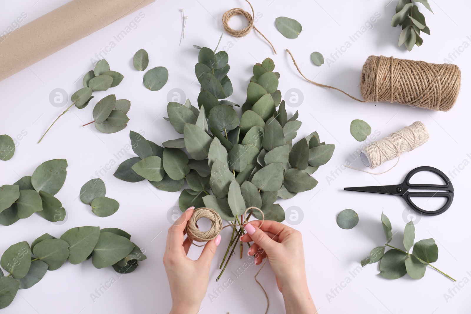 Florist making beautiful bouquet of eucalyptus branches at white table, top view Photo of Florist making beautiful bouquet of eucalyptus branches at white table, top view