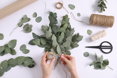 Photo of Florist making beautiful bouquet of eucalyptus branches at white table, top view