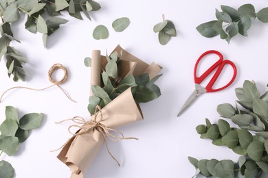 Photo of Florist. Eucalyptus branches, thread, scissors and wrapping paper on white table, flat lay