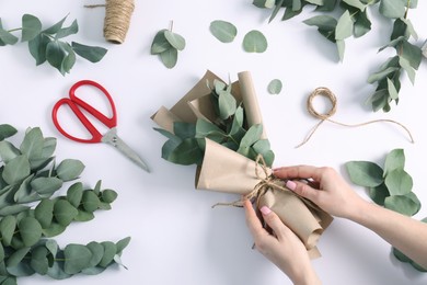Photo of Florist making beautiful bouquet of eucalyptus branches at white table, top view
