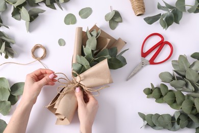 Photo of Florist making beautiful bouquet of eucalyptus branches at white table, top view