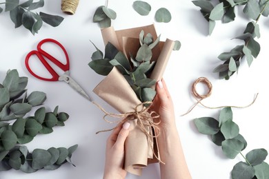 Photo of Florist making beautiful bouquet of eucalyptus branches at white table, top view