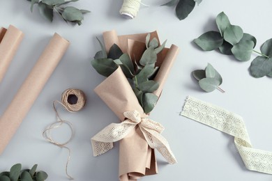Photo of Florist. Eucalyptus branches, threads, ribbon and wrapping paper on white table, flat lay