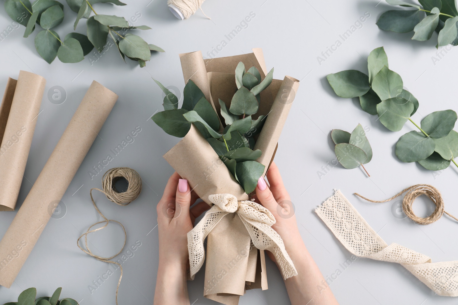 Florist making beautiful bouquet of eucalyptus branches at white table, top view Photo of Florist making beautiful bouquet of eucalyptus branches at white table, top view
