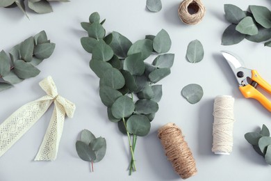 Photo of Florist. Eucalyptus branches, threads, pruner and bow on white table, flat lay