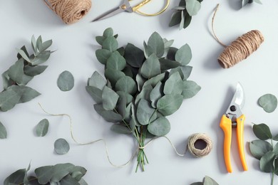 Photo of Florist. Eucalyptus branches, threads, pruner and scissors on white table, flat lay