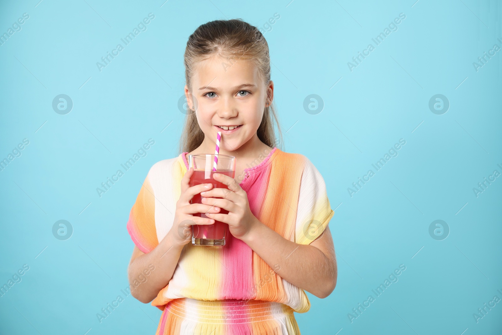 Little girl drinking juice through straw on light blue background Photo of Little girl drinking juice through straw on light blue background