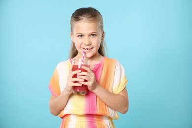 Photo of Little girl drinking juice through straw on light blue background