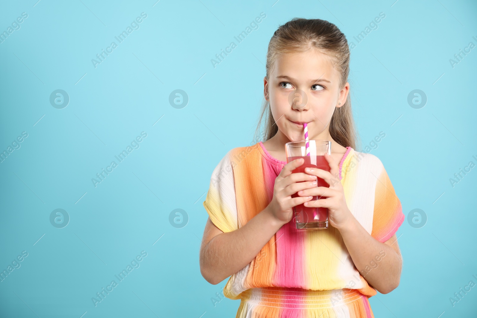 Little girl drinking juice through straw on light blue background, space for text Photo of Little girl drinking juice through straw on light blue background, space for text