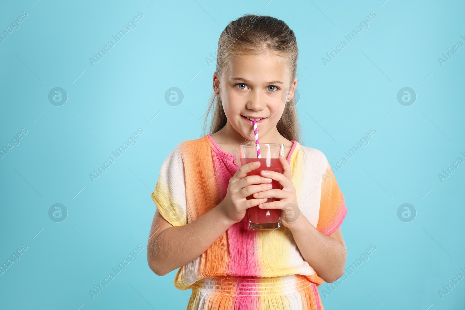 Photo of Little girl drinking juice through straw on light blue background