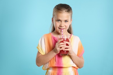 Photo of Little girl drinking juice through straw on light blue background