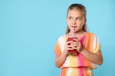 Photo of Little girl drinking juice through straw on light blue background, space for text