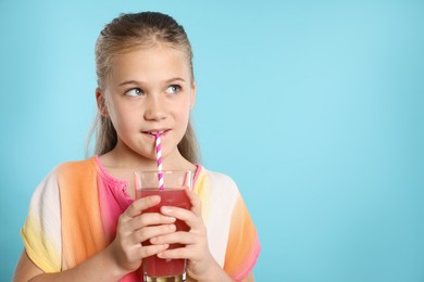 Photo of Little girl drinking juice through straw on light blue background, space for text