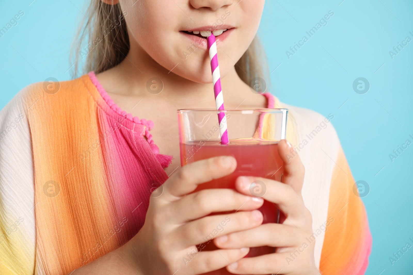 Little girl drinking juice through straw on light blue background, closeup Photo of Little girl drinking juice through straw on light blue background, closeup