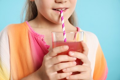 Photo of Little girl drinking juice through straw on light blue background, closeup