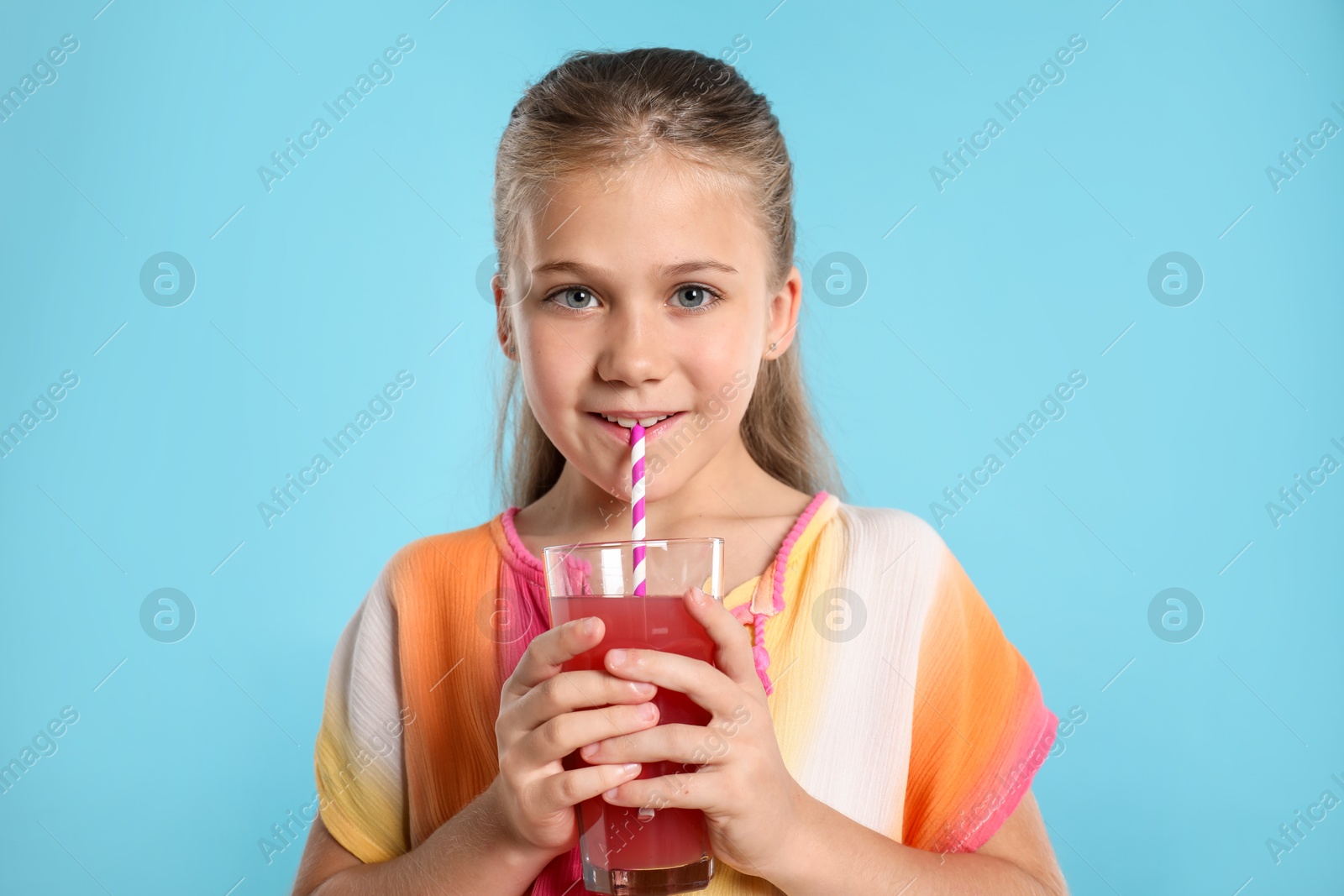 Little girl drinking juice through straw on light blue background Photo of Little girl drinking juice through straw on light blue background