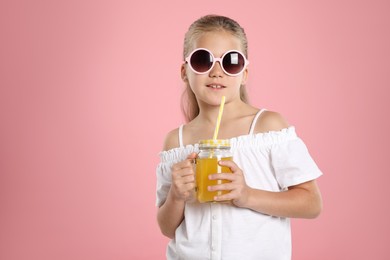 Photo of Little girl with juice and drinking straw on pink background, space for text