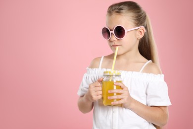 Photo of Little girl with juice and drinking straw on pink background, space for text
