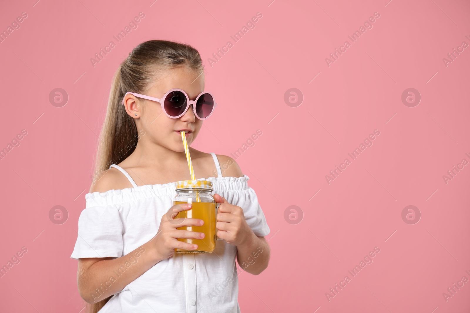 Photo of Little girl drinking juice through straw on pink background, space for text