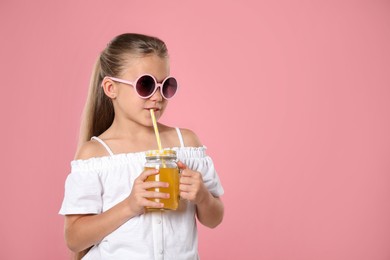 Photo of Little girl drinking juice through straw on pink background, space for text